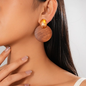 Gros plan de boucles d'oreilles géométriques en bois et résine ambrée sur un modèle