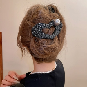 Detail of a large heart-shaped hair claw clip with black crystals and a gray pearl accent