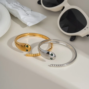 Snake wrap open cuff bracelet in gold and silver with green gemstone eyes on cream background