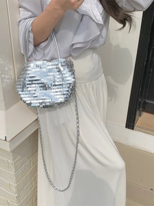 Chic silver sequin tote bag with metal chain strap shown in a stylish outdoor setting
