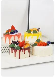 Close-up of four artificial mousse cakes with colorful fruit toppings on a display stand