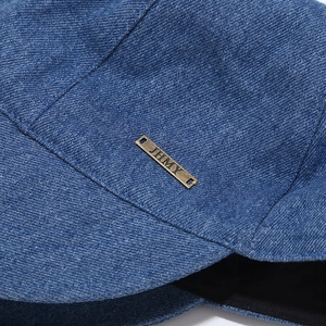 Macro detail of washed denim fabric texture and vintage bronze metal logo on the sun hat