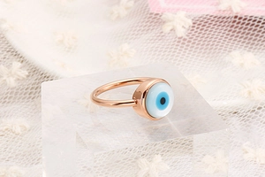 Detail of rose gold evil eye ring displayed on white lace with Mediterranean aesthetics