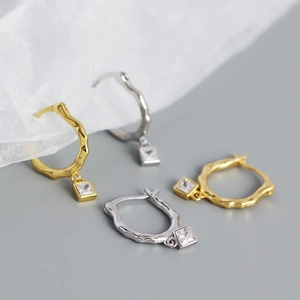 Detailed shot of irregular gold and silver hoop earrings with square zircon pendants