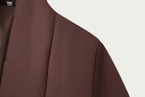 Detailed view of the shoulder seam and padded fabric of a dark brown quilted winter jacket