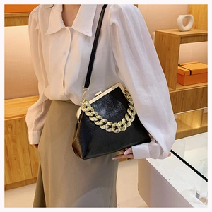Detail of black pebbled leather handbag with chunky gold chain and metal frame closure