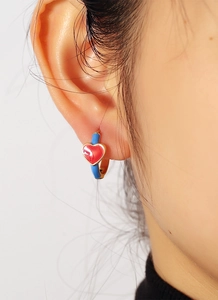 Close-up of a model wearing gold earrings with blue enamel and red heart details