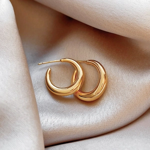 Macro shot of chunky gold hoop earrings on champagne silk fabric with mirror finish