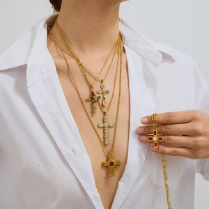 Détail de colliers en or superposés avec pendentifs croix et pierres colorées