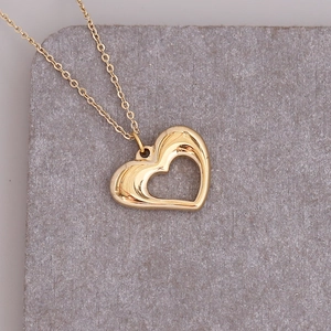 Detailed view of a gold hollow heart pendant necklace on a gray textured stone