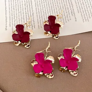 Elegant matte floral earrings with golden branches and deep red petals on a magazine page