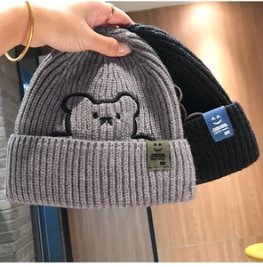 Close-up of knit beanies with bear embroidery and smile patch showing fabric texture