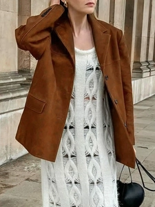 Détail d'une veste en daim caramel à col revers portée avec une robe en maille blanche