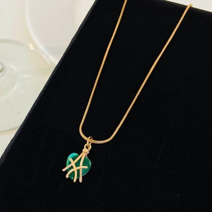 Foto macro de collar con colgante de corazón verde y detalles dorados en caja de regalo