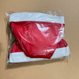 Detailed view of red and white plush Christmas hat folded in transparent plastic packaging