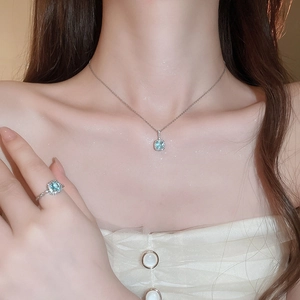 Close-up of elegant silver necklace and ring set with square light blue gemstones on a model