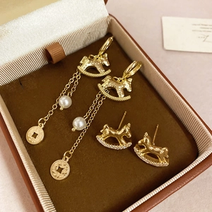 Détail des boucles d'oreilles cheval à bascule dorées avec pompons et perles en boîte