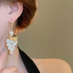 Detailed view of French leaf pearl grape tassel earrings worn by a model in warm light