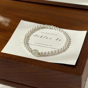 Detail of white pearl bracelet with a green jade bead and golden metal spacers