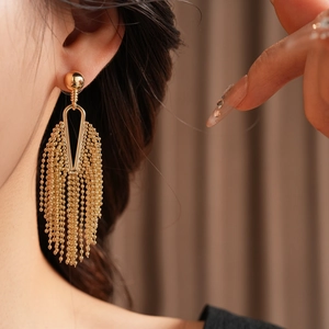 Close-up of elegant gold tassel earrings with bead chains on model's ear
