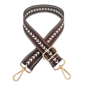 Detail of adjustable brown nylon strap with white herringbone pattern and gold metal hooks