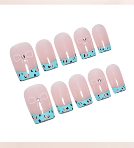 Détail de faux ongles léopard français avec motifs de nœuds et petits strass brillants