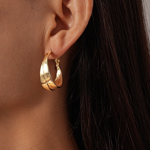 Close-up of golden hollow layered hoop earrings on model showing double twist design