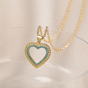 Gros plan du pendentif cœur évidé plaqué or avec zircons turquoise sur une chaîne fine