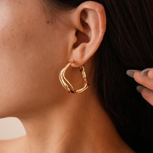 Close-up of gold-finish irregular wavy hoop earrings worn by a model in profile