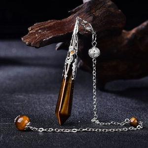 Macro detail of Tiger Eye hexagonal prism pendulum with intricate silver chain on dark wood