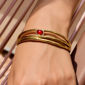 Dettaglio di un bracciale a tre fili in acciaio dorato con gemma rossa ovale incastonata