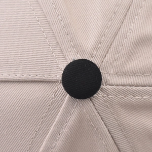 Detailed top view of a beige cotton baseball cap with black button and six-panel stitching