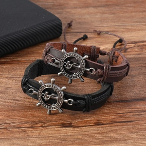 Detail view of woven leather bracelets with silver anchor and rudder charms on wood