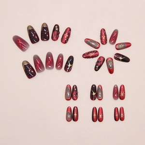 Detail of dark red and black press-on nails featuring cat eye effect and gold star patterns