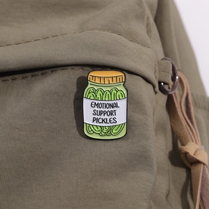 Detail of Emotional Support Pickles enamel pin on a green canvas backpack fabric