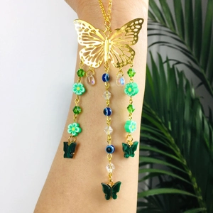 Detail of gold butterfly car pendant with green flowers and blue beads on a model's wrist