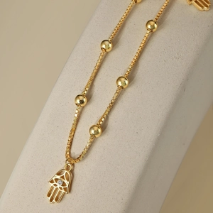 Gros plan du pendentif main de Hamsa doré sur une chaîne à billes sur fond de pierre