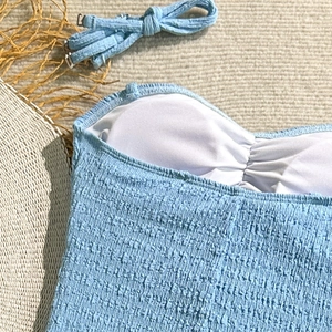 Detail of light blue crinkled swimsuit fabric featuring metal buckle and soft inner lining