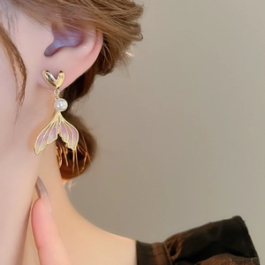 Detail of elegant gradient fishtail pearl earring worn on ear with golden heart stud