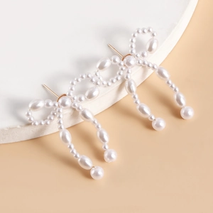 Detailed view of handmade pearl bow earrings with white beads and gold needle posts