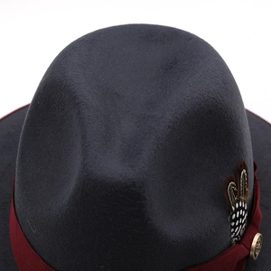 Detailed close-up of dark grey wool felt fedora with ribbon, feathers and metal badge