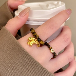 Detailed shot of tiger eye beaded ring with golden tiger and coin charms on a hand