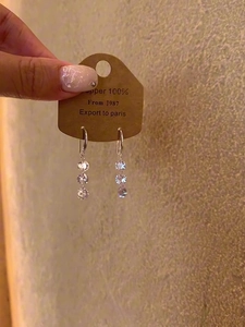 Detail of silver drop earrings with triple zircons held on a brown paper card tag