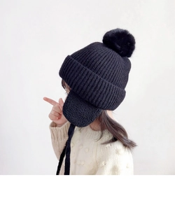 Detail view of children's black knitted hat featuring soft earflaps and a large pompom