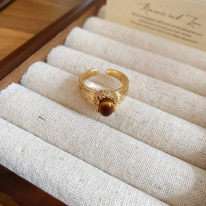 Macro view of a gold-plated tiger eye ring with crystal pavé on a beige velvet box