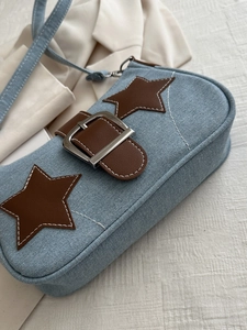Detail of light blue denim shoulder bag with brown leather stars and silver buckle