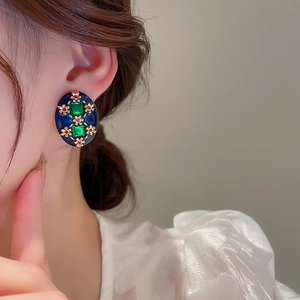 Detail of vintage oval earrings with blue enamel and green gems on female model