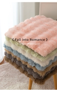 Pila di spessi cuscini in peluche in vari colori tenui su uno sgabello di legno