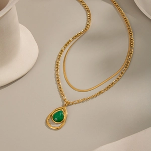 Detail of layered gold snake and O-chain necklace with green teardrop gemstone pendant