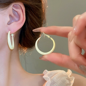 Close-up of creamy yellow round hoop earring worn by model and held by hand